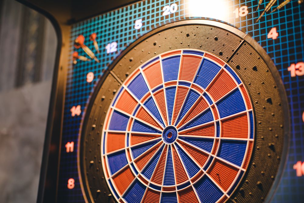 Eine beleuchtete Dartscheibe mit steckenden Pfeilen in der Bar