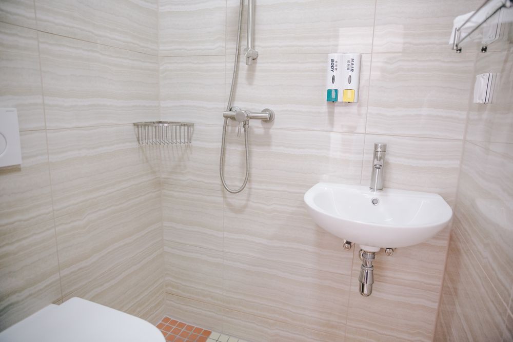 Ein eigenes Badezimmer in hellem Steinfliesen-Look mit begehbarer Dusche und Waschbecken