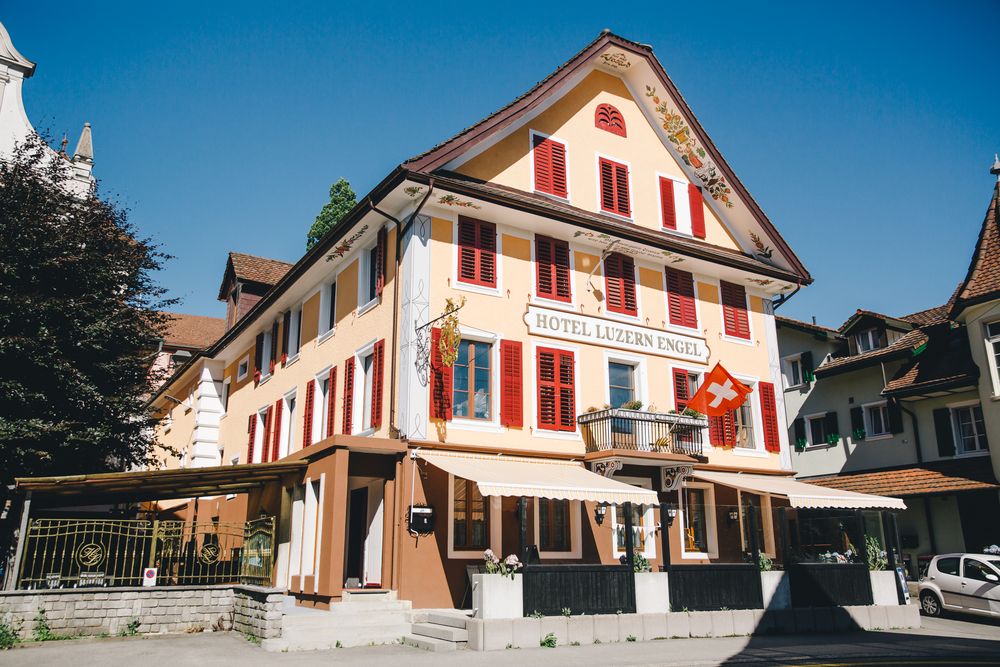 Die bemalte Fassade des Hotel Luzern Engel im Sonnenlicht mit geöffneten roten Fensterläden über der Dorfstrasse