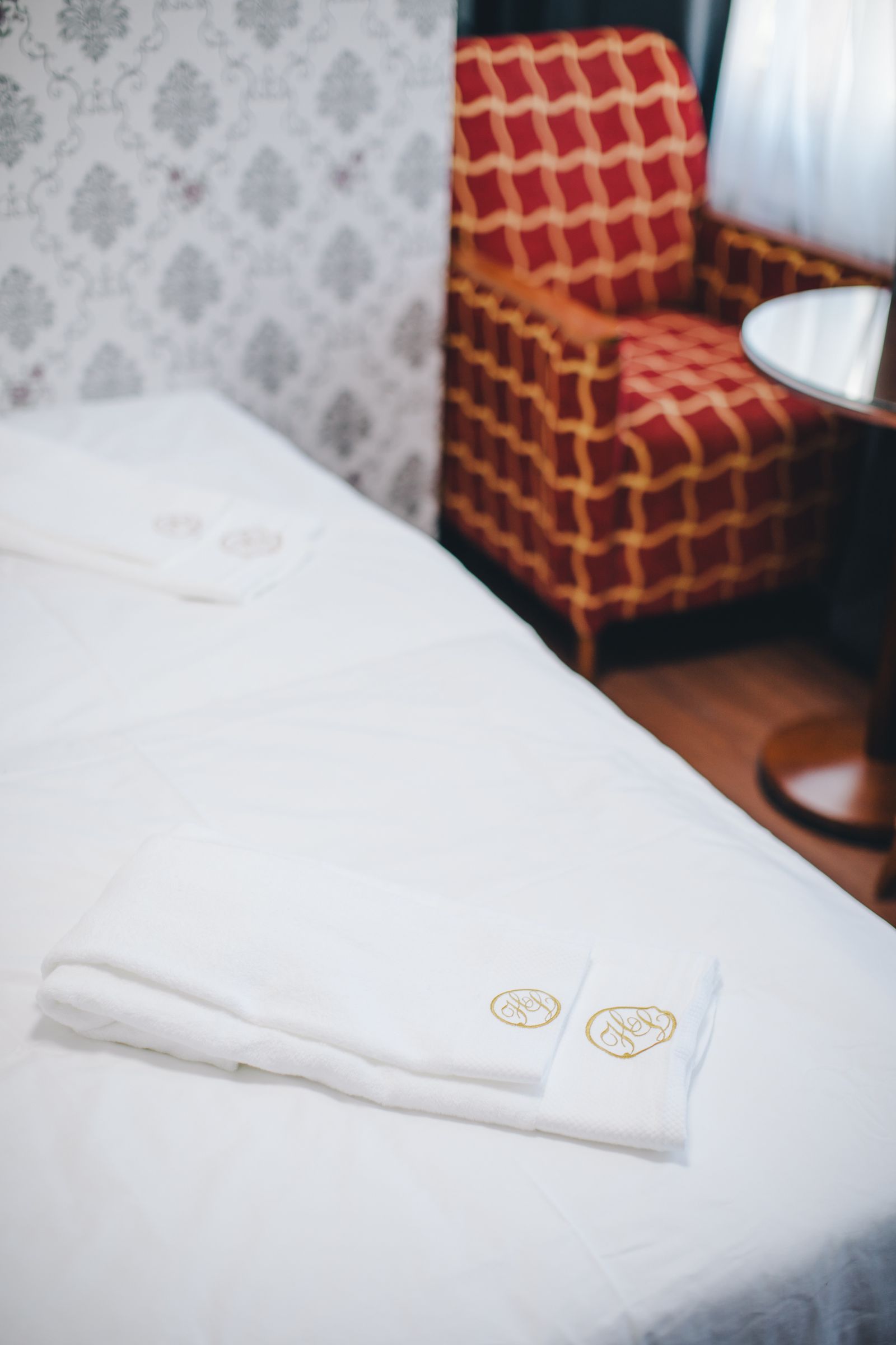 Frische Tücher auf einem gemachten Bett neben rotem Sessel und Leselampe