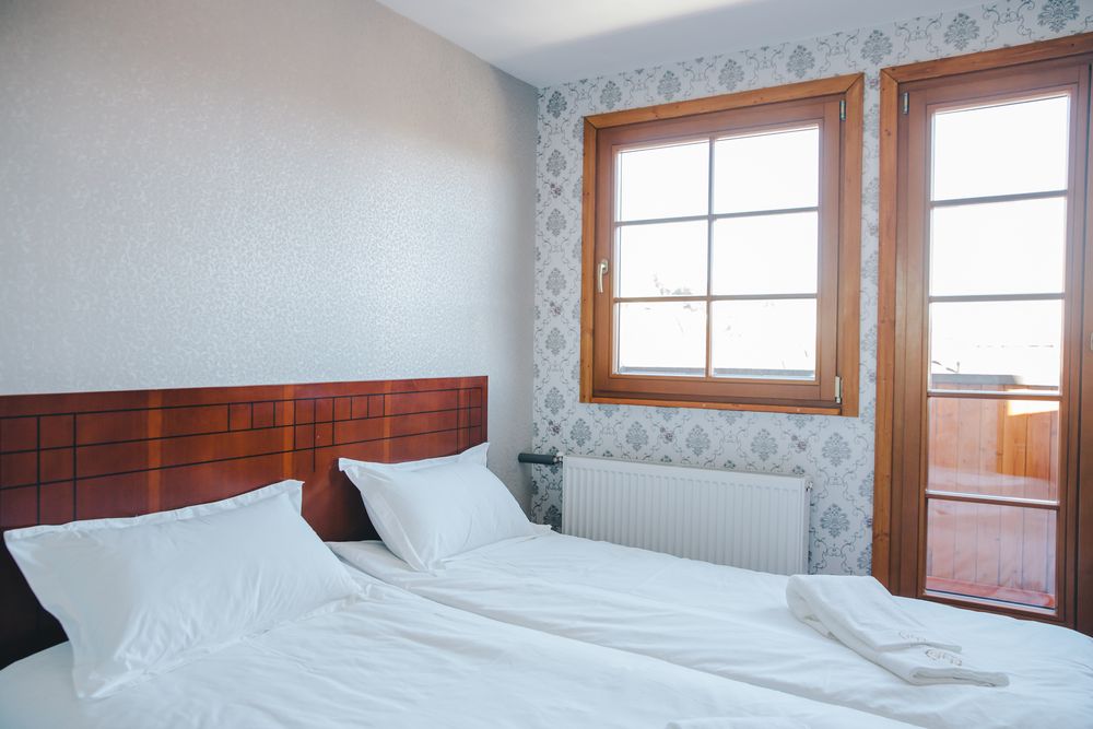 Ein Doppelzimmer mit hölzernem Kopfteil und frischer weisser Bettwäsche, die Balkontür zum Licht geöffnet