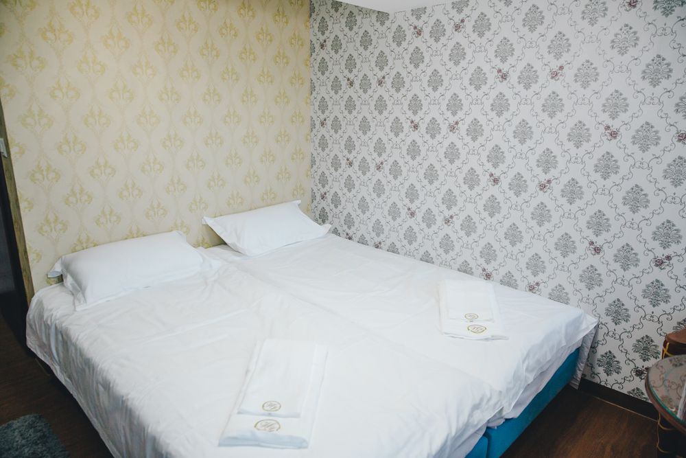 Ein Doppelbett mit weisser Bettwäsche und gefalteten Tüchern vor gemusterter Tapete