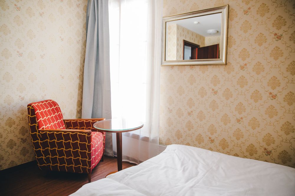 Ein Einzelzimmer mit einem Bett, einem Sessel und einem Spiegel am Fenster