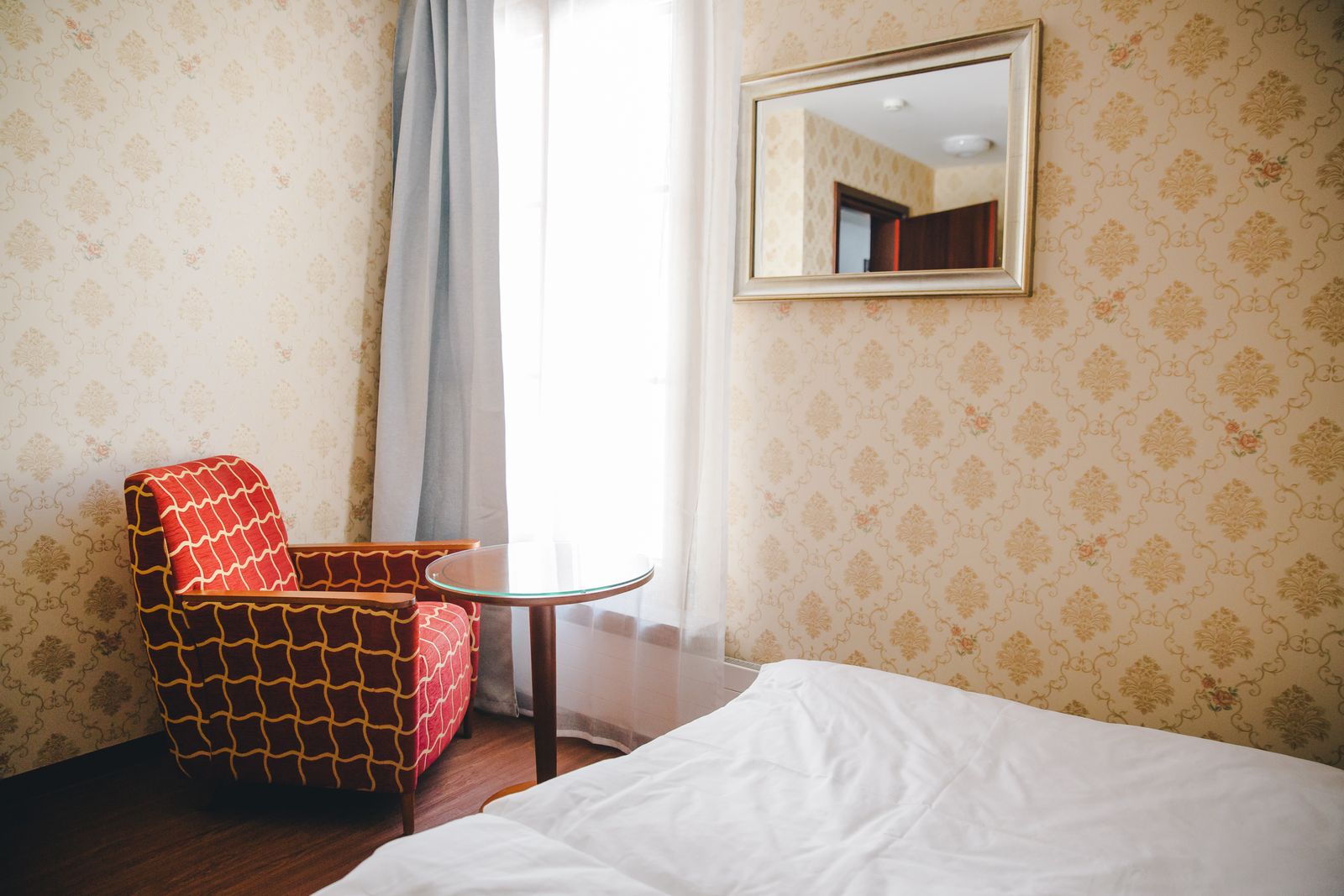 Ein Einzelzimmer mit einem Bett, einem Sessel und einem Spiegel am Fenster