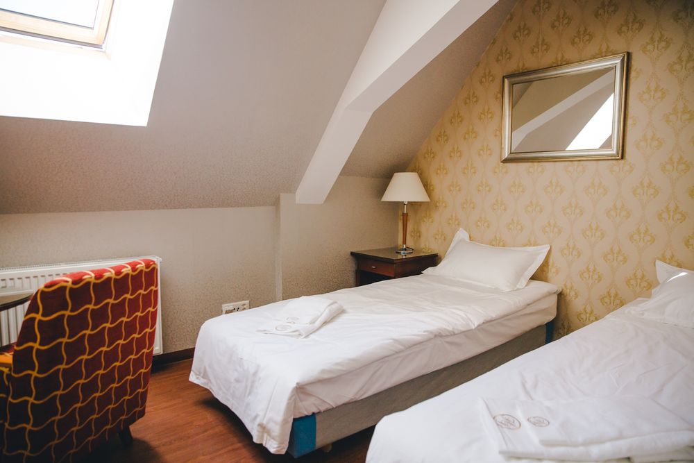 Ein helles Zimmer unter dem Dach mit separaten Betten und einem rot gemusterten Sessel