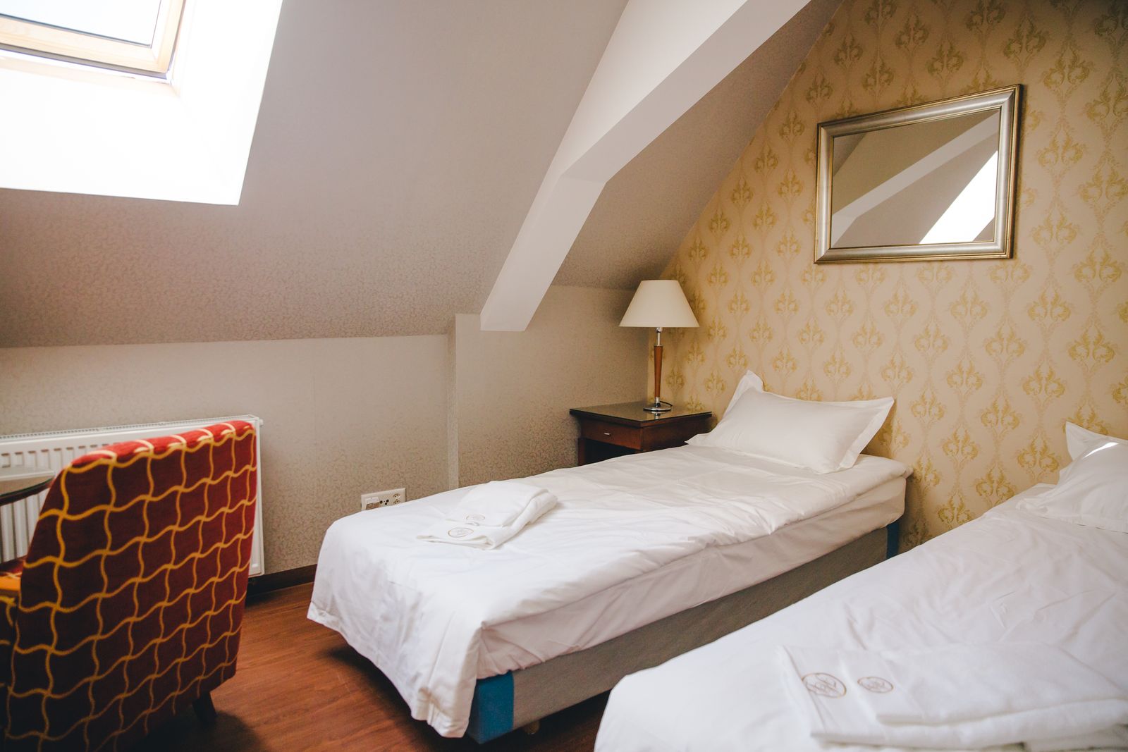 Ein helles Zimmer unter dem Dach mit separaten Betten und einem rot gemusterten Sessel