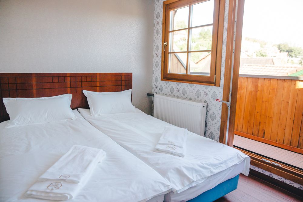 Ein Zweibettzimmer mit zwei nebeneinanderstehenden Betten und Tür zum Holzbalkon